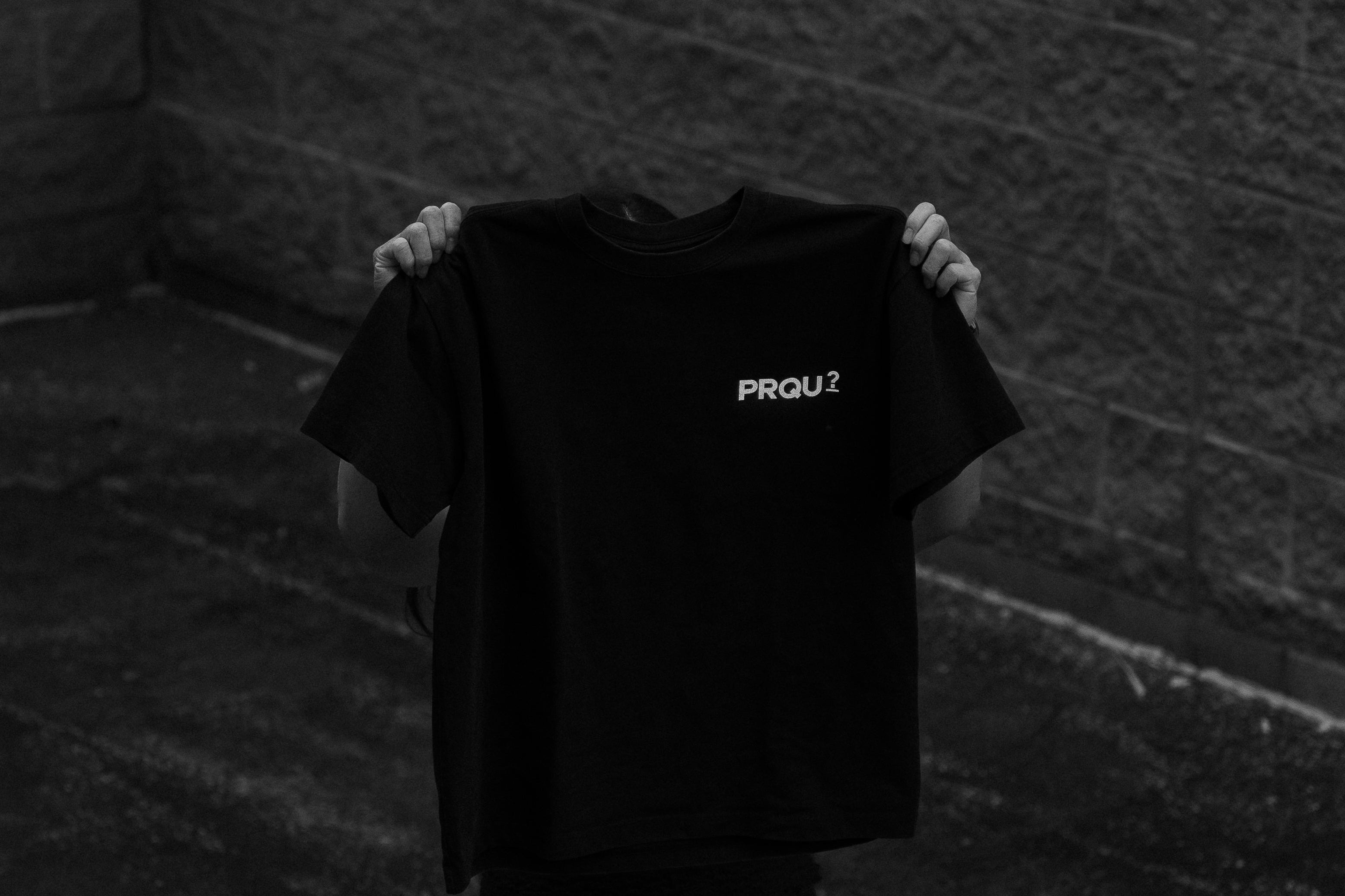 Person holding a black t-shirt with text in a dark room